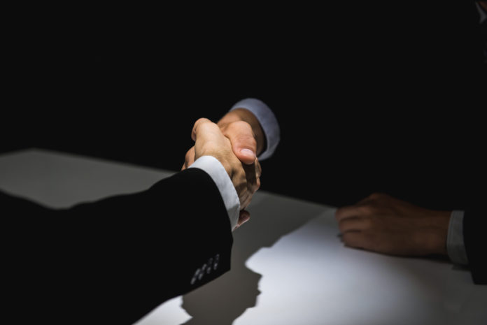 Business partners making handshake in dark shadow