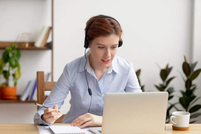 Business woman wearing headphones watching video webinar write notes