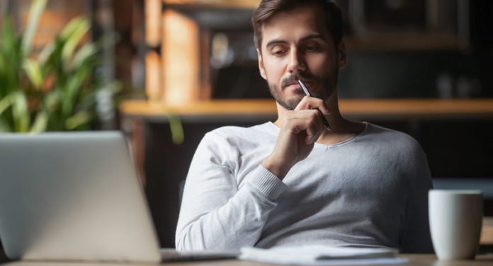 Pensive male thinking over problem solution working on laptop
