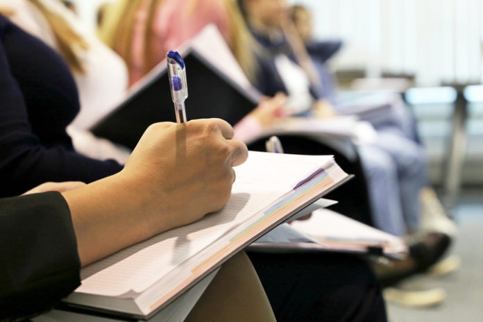 Women sitting in a row in a conference room, female hand with pen writing in a notepad
