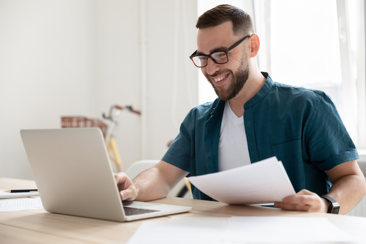 Happy young businessman in eyeglasses working on computer.