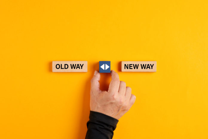 Male hand holds a wooden cube with arrow icon between the options of old way or new way.