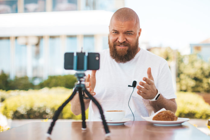 Young bearded man speaks in front of camera - blogging (vlogging) and technology concept