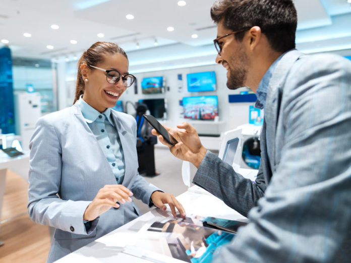 Young multicultural couple looking for new smart phone to buy. Woman looking at catalog while man holding smart phone.